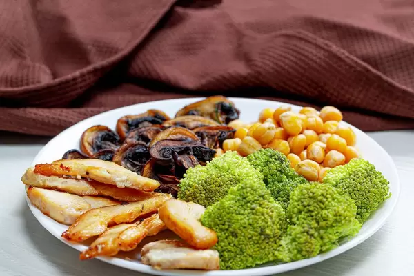 Broccoli with chickpeas, mushrooms and chicken on a white plate