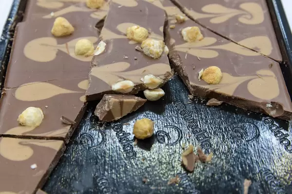 Broken Caramel chocolate with pattern and whole hazelnuts, on a dark tray