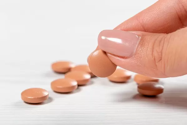 Brown pills on a white wooden background and one in a woman's hand (Flip 2019)