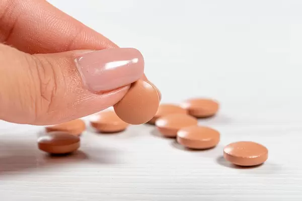 Brown pills on a white wooden background and one in a woman's hand