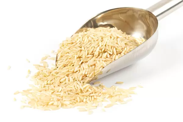 Brown rice in metal scoop on white