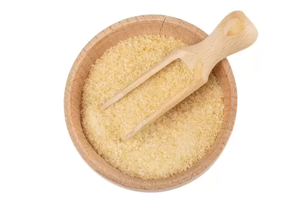 Brown sugar in a wooden bowl with a scoop, top view