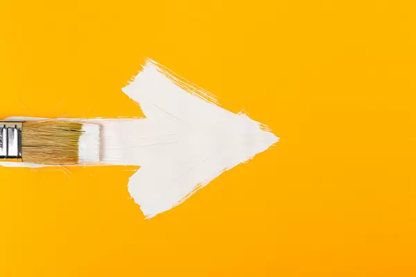 Brush draws an arrow on orange with white paint