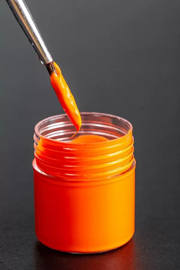 Brushes with orange paint with a jar of gouache paint on a dark background