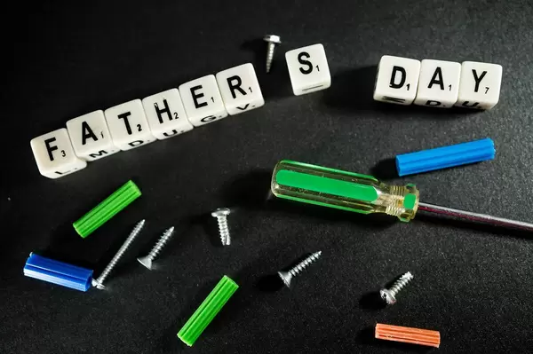 Buchstabenwürfel erinnern an den Vatertag "Father's Day", umgeben von Schrauben und Werkzeuge auf einem schwarzen Untergrund