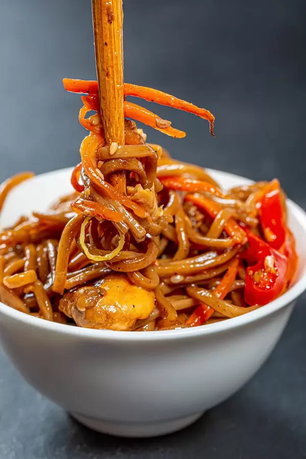 Buckwheat noodles (soba) in a white bowl with sauce, vegetables and chopsticks on black background