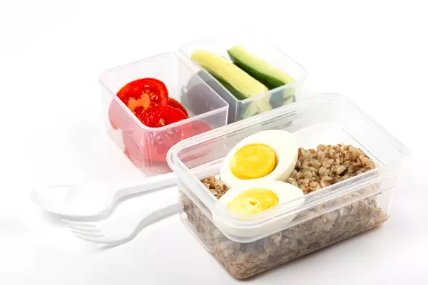 Buckwheat porridge with boiled eggs, pieces of fresh cucumbers and tomatoes in plastic containers