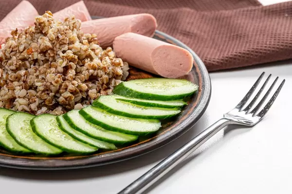 Buckwheat porridge with cucumber slices and sausages on a plate closeup (Flip 2019)