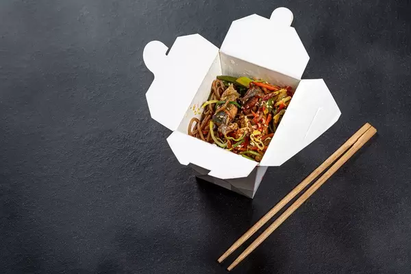 Buckwheat soba noodles with vegetables and fish in a cardboard box with chopsticks on a black background