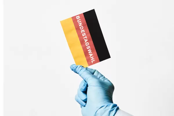 Bundestagswahl in der Corona-Pandemie: Hand mit Einmalhandschuh hält Zettel mit deutscher Flagge