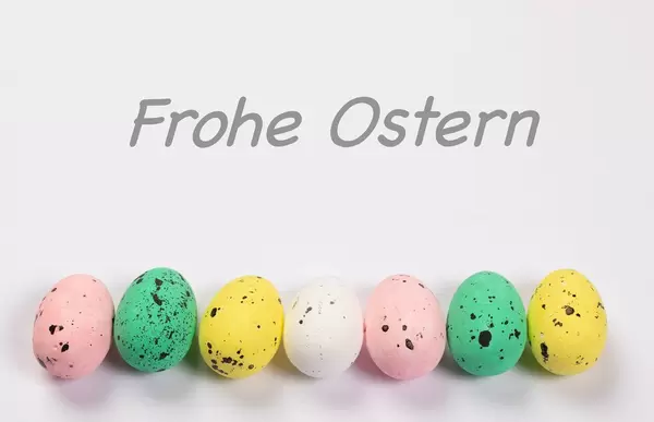 Bunt bemalte Ostereier liegen in einer Reihe unter Text FROHE OSTERN vor weißem Hintergrund