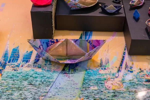 Bunt bemalte Papierschiffe in verschiedenen Größen auf künstlerischem Untergrund