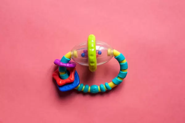 Bunte Babyrassel aus Plastik für Neugeborene vor rosarotem Hintergrund