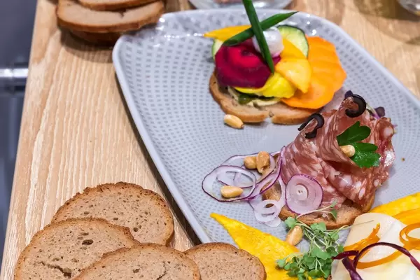 Bunte Brotzeit: Wurst mit Kräutern, Zwiebeln und Nüssen, neben garnierten Brotscheiben auf einem Tablett