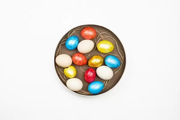 Bunte Eier zu Ostern auf einem braunen Teller vor weißem Hintergrund. Aufnahme von oben