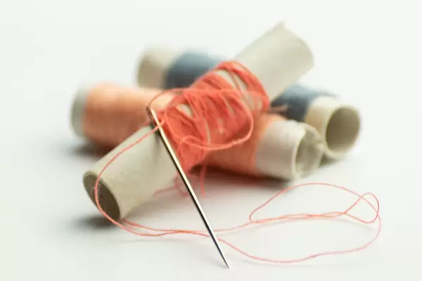 Bunte Fäden mit Nadel vor weißem Hintergrund