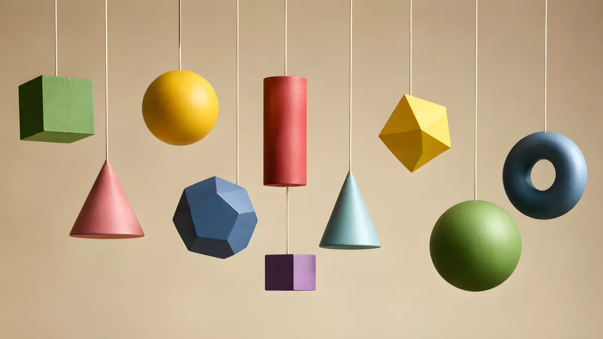 Bunte geometrische Formen hängen an Fäden vor beigem Hintergrund