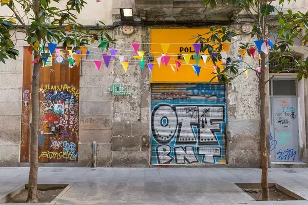 Bunte Girlanden zwischen Bäume gespannt, vor Graffiti an der spanischen Straße Carrer de la Riera Baixa in Barcelona