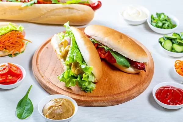 Bunte Hotdogs mit verschiedenen Saucen und gesunden Beilagen, auf einem gedeckten Mittagstisch