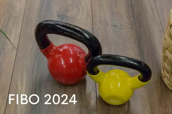 Bunte Kettlebells in verschiedenen Gewichten, stehen auf einem Holzparkett, neben dem Bildtitel "Fibo 2024"
