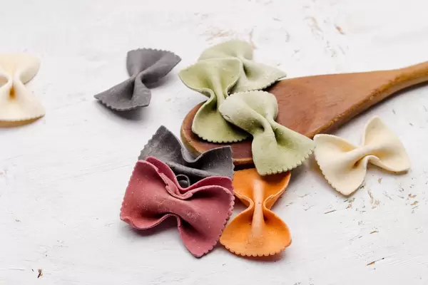 Bunte Nudeln mit Kochlöffel vor weißem Hintergrund