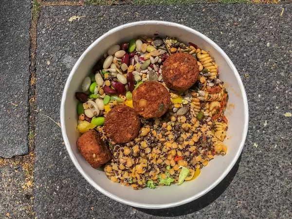 Bunte Salatmischung mit Pasta, vegetarischen Fleischbällchen und Bohnen, in einer Pappschale zum Mitnehmen