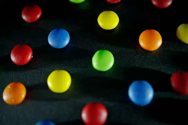 Bunte Smarties, Süßigkeiten aus Schokolade mit farbiger Glasur verteilt auf dunklem Untergrund