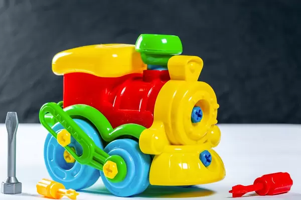 Bunte Spielzeug-Lokomotive aus Kunststoff mit Schraubenschlüsseln auf weißem Tisch