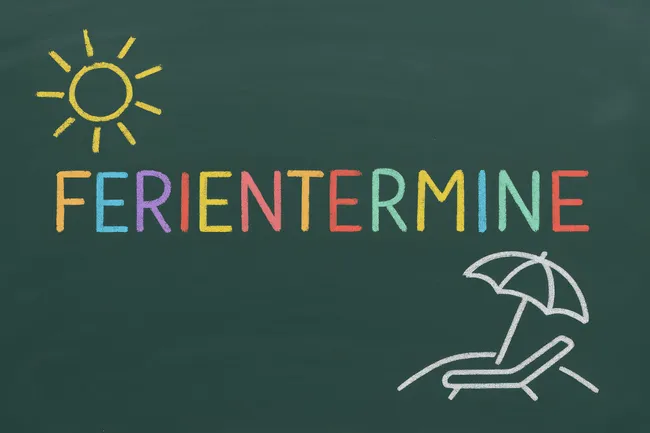 Bunte Tafelanschrift 'Ferientermine' mit Sonnensymbol und Liegestuhl