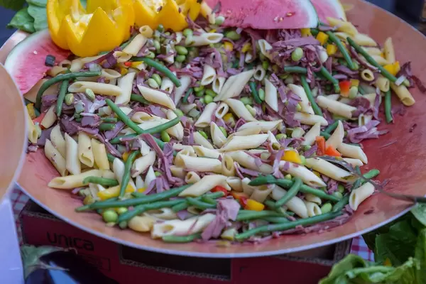 Bunter Penne-Nudelteller als exotisches Mittagessen, mit Bohnen, Schinken, Paprika und Wassermelone