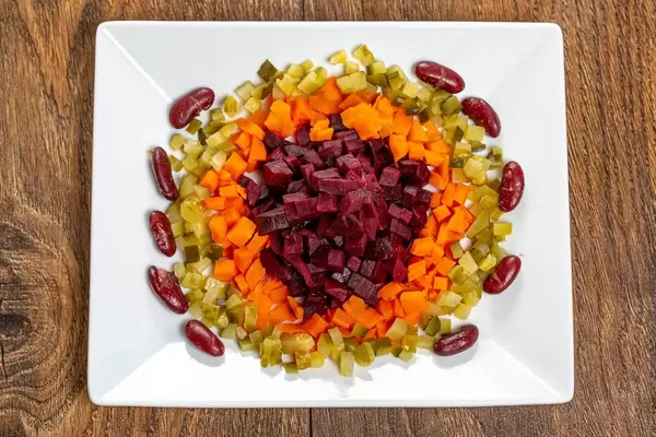 Bunter Salat aus Bohnen, Gewürzgurken, Karotten und Rote Bete auf weißem Teller in obene Aufnahme