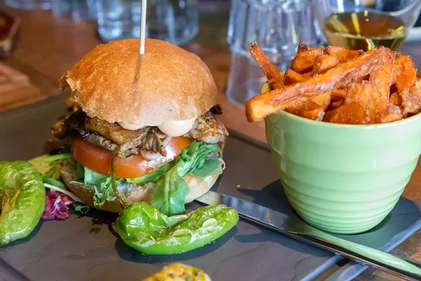Burger auf einem Holzspieß, mit Tomaten, Salat, Fleisch und Sauce, neben grünen Pepperoni und Süßkartoffel-Pommes im Restaurant