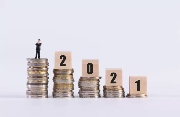 Businessman, stack of coins and wooden cubes with 2021 text on white background