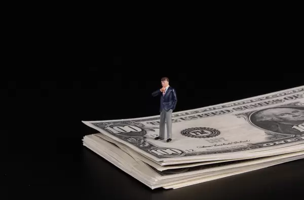 Businessman standing on a stack of 100 Dollar banknotes