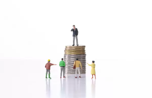 Businessman standing on a stack of coins in front of group of people