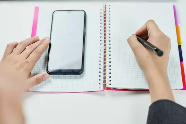 Businesswoman checking calendar on her smartphone and writing notes on the notepad