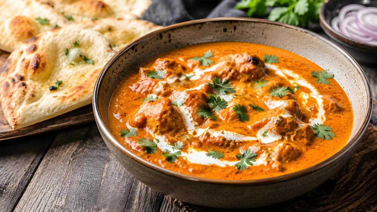 Butter Chicken in Schüssel mit Naan und Koriander