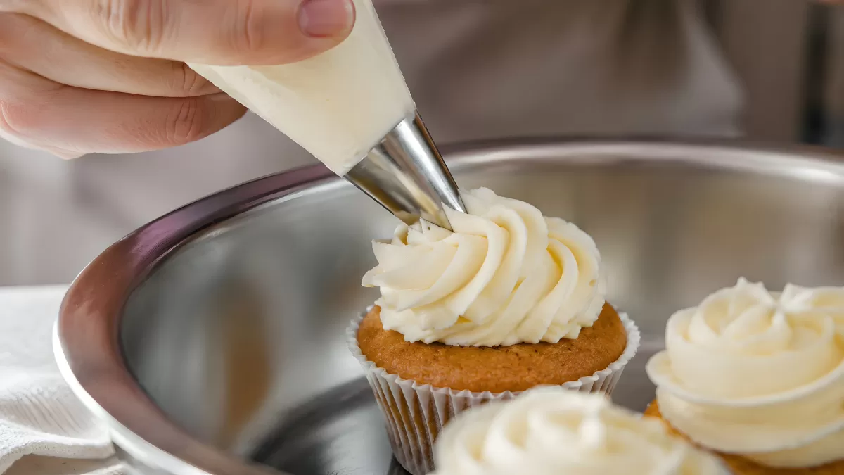 Buttercreme auf Cupcakes mit Spritzbeutel auftragen