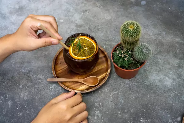 Cactus next to a Glas of Burnt Orange Cold Brew Coffee with a Person touching a Paper Straw