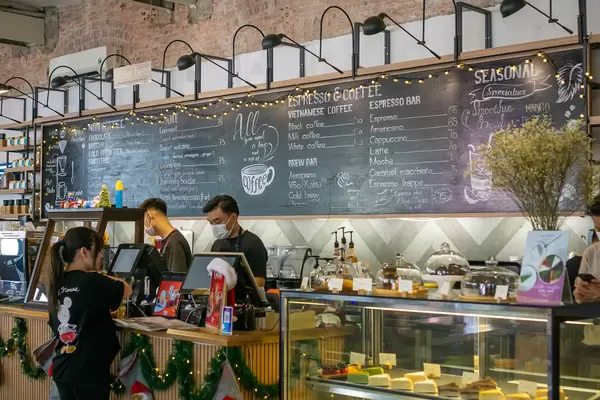 Cafe Staff wearing Facemasks at a Counter with large Menu on a Blackboard decorated with Christmas String Lights