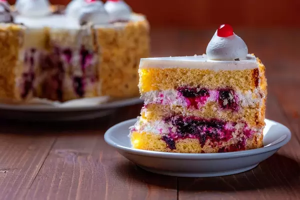 Cake with white cream and black currant inside with a cut off piece