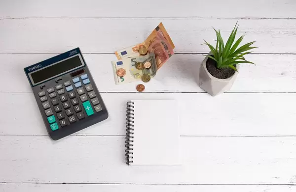 Calculator, notebook and money on white wooden table