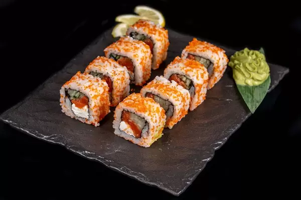 California set rolls with salmon, wasabi sauce and lemon slices on a dark background