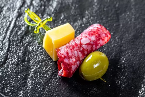 Canape mit Käsesalami und grüner Olive auf schwarzem Steinhintergrund