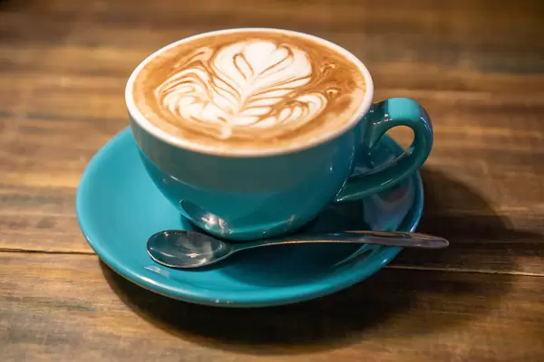 Cappuccino in Keramiktasse mit Löffel und Untertasse auf Holztisch Nahaufnahme