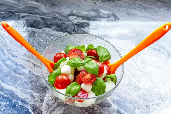 Caprese-Salat in einer Glasschale mit zwei orangen Salatlöffeln
