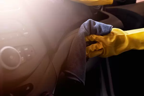 Car cleaning service - hand in rubber gloves cleaning car interior panel with a cloth