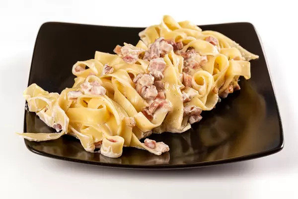 Carbonara pasta with creamy sauce, bacon and ham on a black plate