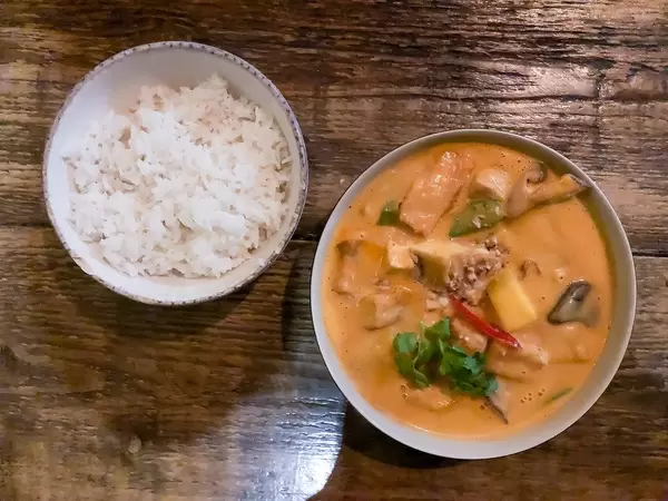 Càri Xoài: scharfes vietnamesisches Gericht mit Bio-Tofu in rotem Kokoscurry mit Mangogeschmack, zusammen mit Süßkartoffeln, Kartoffeln, Shiitake-Pilzen, Zuckererbsen, Cashewkernen, frischer Mango und einer Schüssel Duftreis. Aufnahme von oben