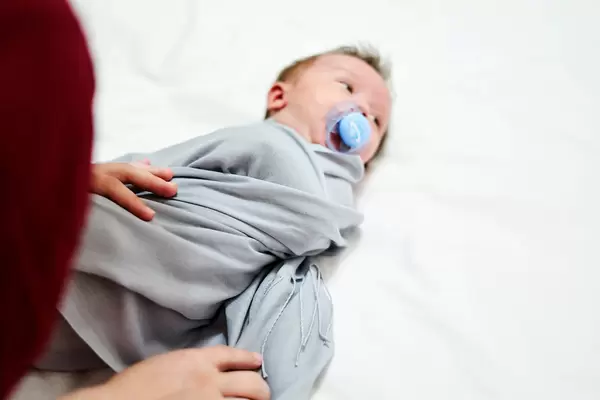 Caring mother wrapping her little 1-month-old baby boy with blanket on changing table
